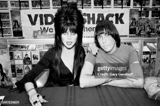 Horror host and actress Cassandra Peterson, in costume as 'Elvira,' and musician Johnny Ramone pose together during an appearance at Video Shack, New...