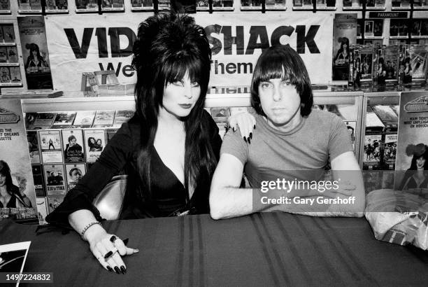 Horror host and actress Cassandra Peterson, in costume as 'Elvira,' and musician Johnny Ramone pose together during an appearance at Video Shack, New...