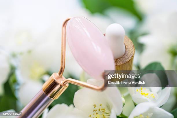 natural beauty cosmetic product, face serum or essential oil and rose quartz jade facial roller for skin care on white and green bokeh jasmine flowers background. - white rose flower spa stock-fotos und bilder
