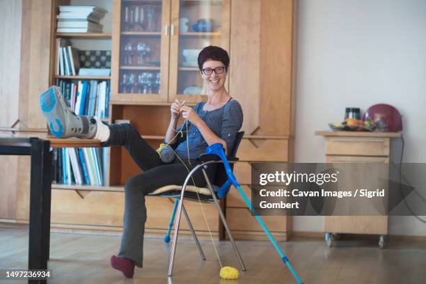 woman resting broken leg on table and knitting at home - women in suspenders stock-fotos und bilder