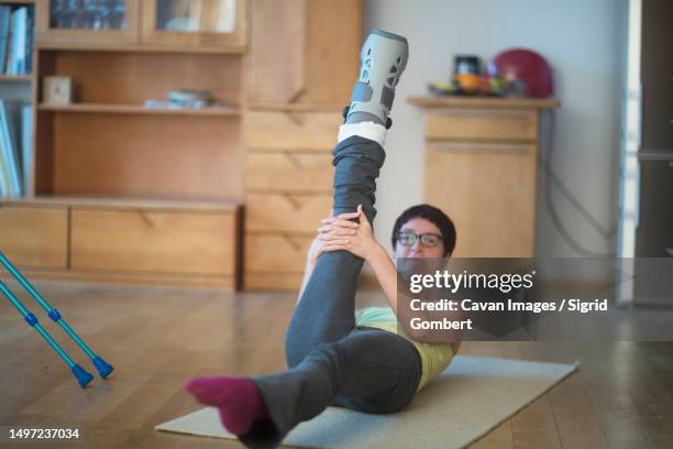 woman doing stretch exercise with a broken leg - gebrochenes bein stock-fotos und bilder