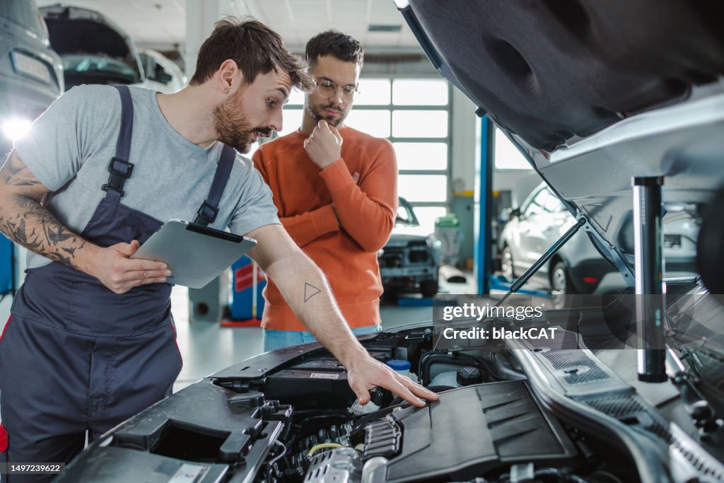 Customer and automotive technician talking about the car problem in a workshop