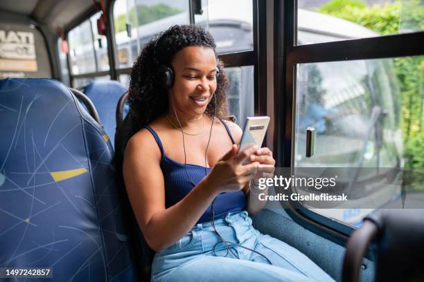 joven sonriente viendo un video en streaming en su teléfono en un autobús - vehículo comercial terrestre fotografías e imágenes de stock