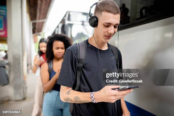 young man watching a video on his phone while waiting for a bus - young man listening to music on smart phone outdoors stockfoto's en -beelden