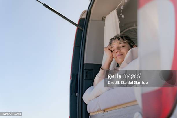 a girl wakes up in her cozy camper and enjoying the scenery with the rear door open, wheels of adventure - lieferwagen stock-fotos und bilder