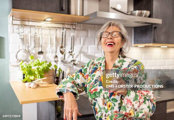 senior woman in kitchen drinks fresh organic juice - ems fitness stock-fotos und bilder