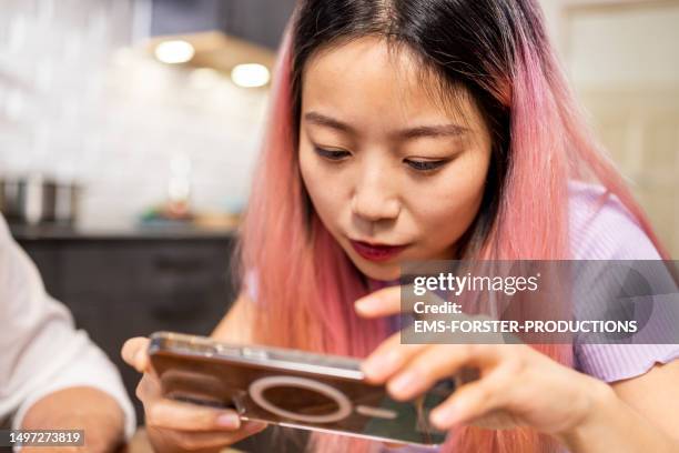 chinese girl with pink dyed is using her smart phone in kitchen and is excited. - fake news stock-fotos und bilder