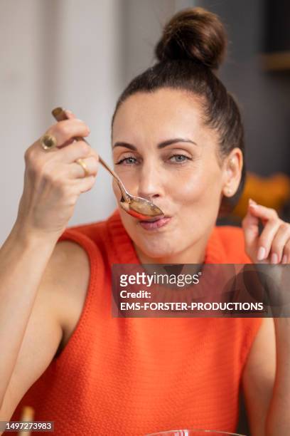 portrait of mature woman with dark hair bun is eating nothing from a empty spoon and looking at camera while intermittent fasting. - ems fitness stock-fotos und bilder
