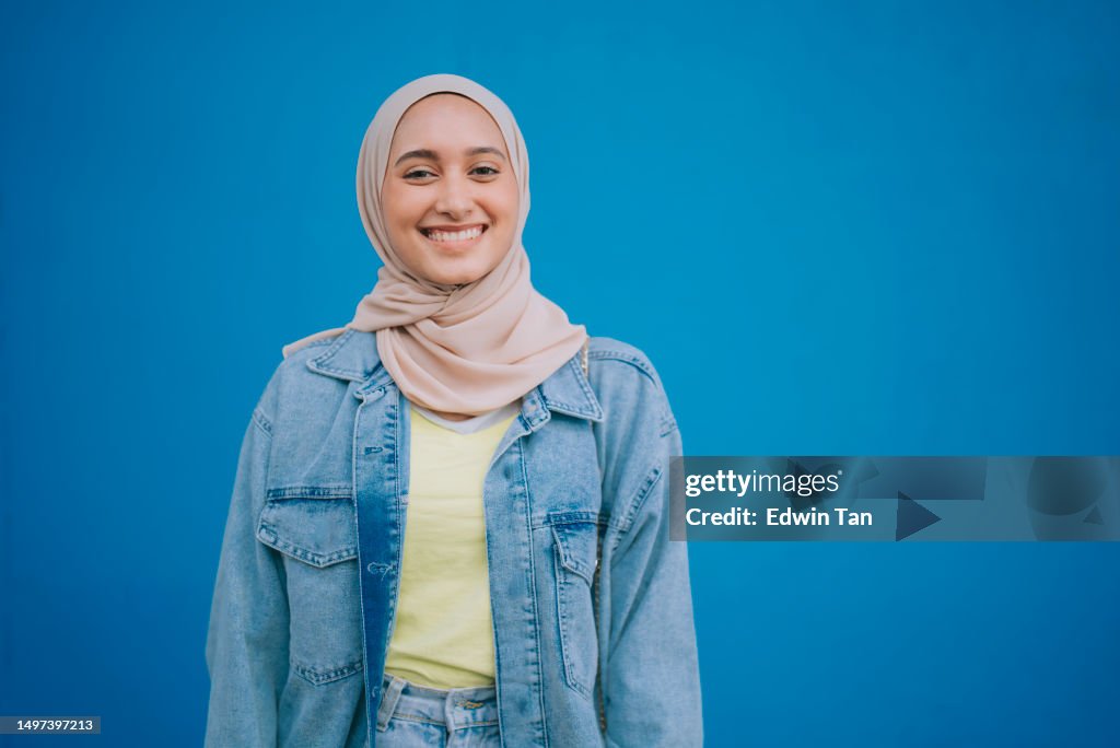 Porträt asiatische malaiische Frau mit Hijab, die lächelnd vor blauer Wand in die Kamera schaut