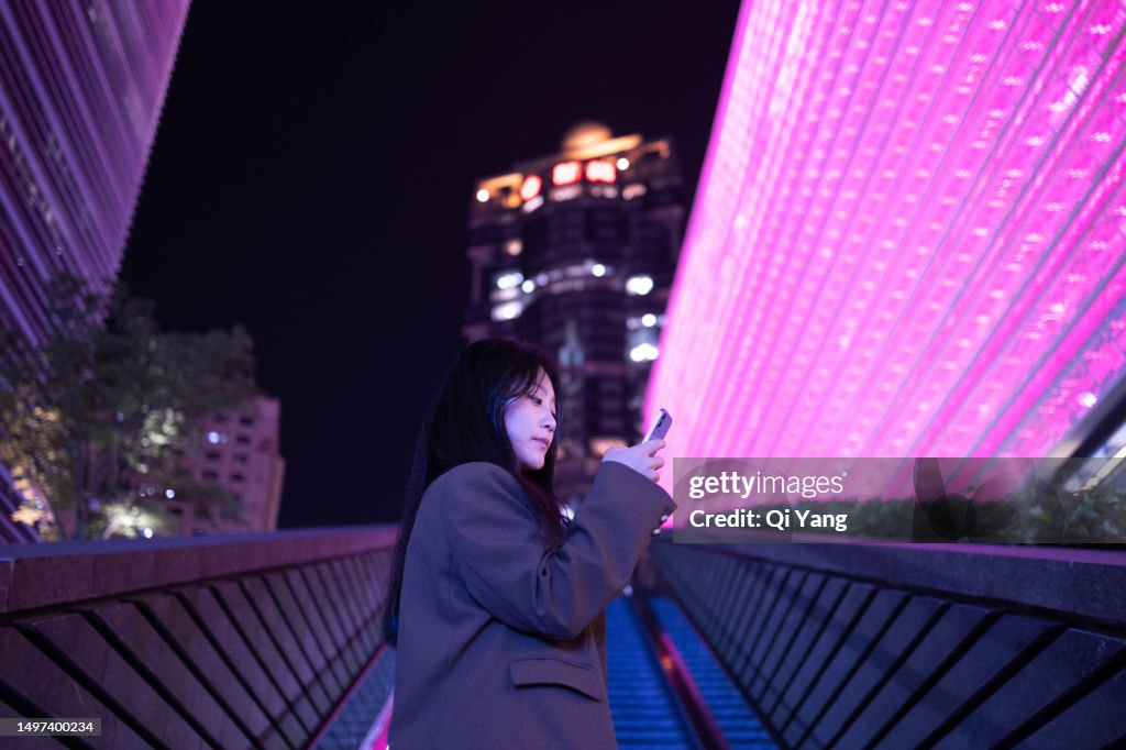 Asian businesswoman using smartphone standing near an escalator