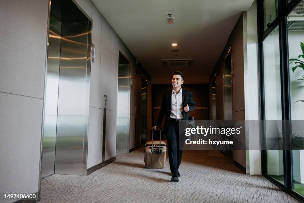 asian businessman with suitcase walking through hotel lift lobby - pulling stock pictures, royalty-free photos & images