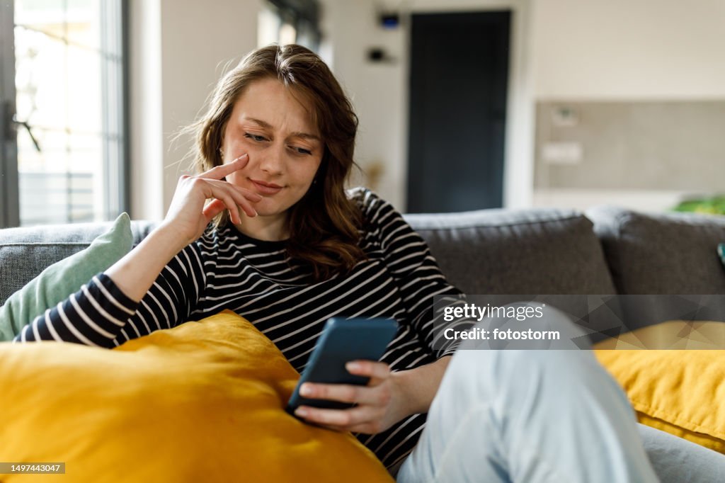Young woman lounging on the sofa and scrolling online via smart phone