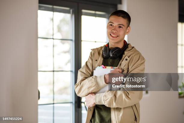 charmanter teenager, der in einem raum steht, schulbücher hält und selbstbewusst lächelt - middle school stock-fotos und bilder