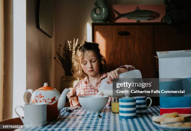 a little girl pours milk on her breakfast cereal in a morning dining table scene - good morning stock pictures, royalty-free photos & images