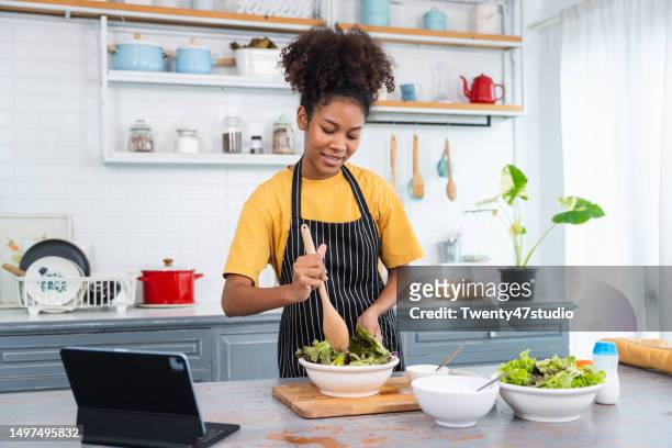 young black woman food blogger making a salad while live streaming at home - dressing room stock-fotos und bilder