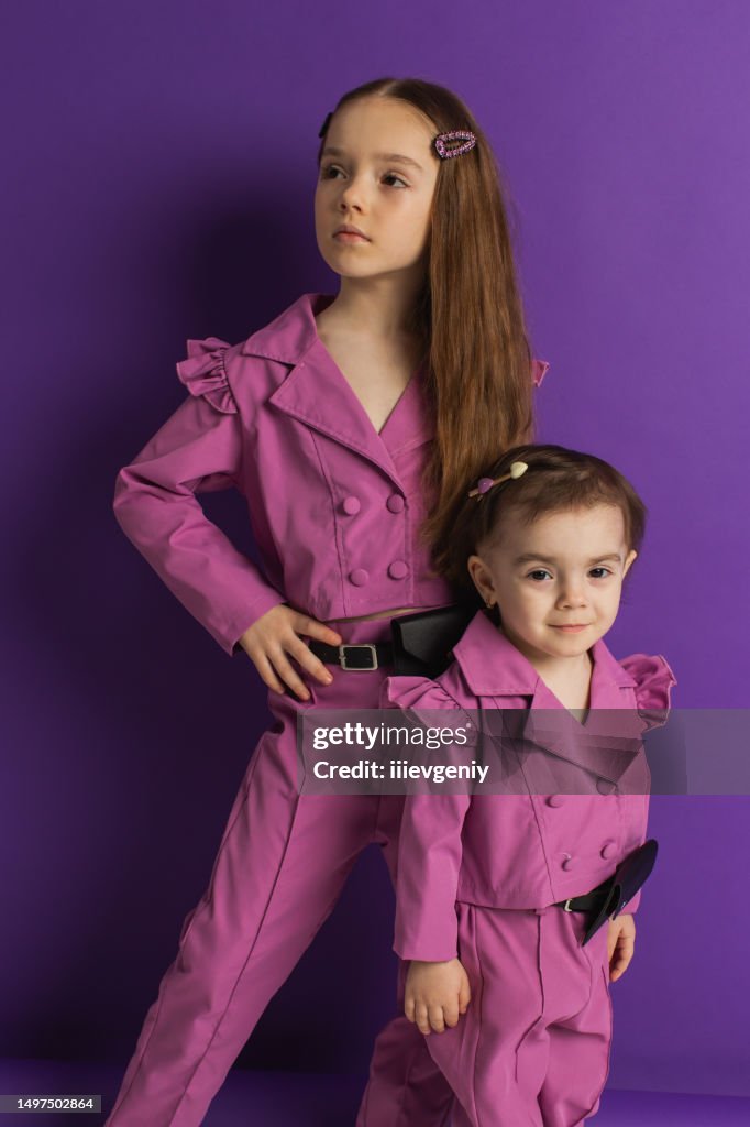 Two blonde girls in purple suit on violet background. Child. Childhood. Summer fashion