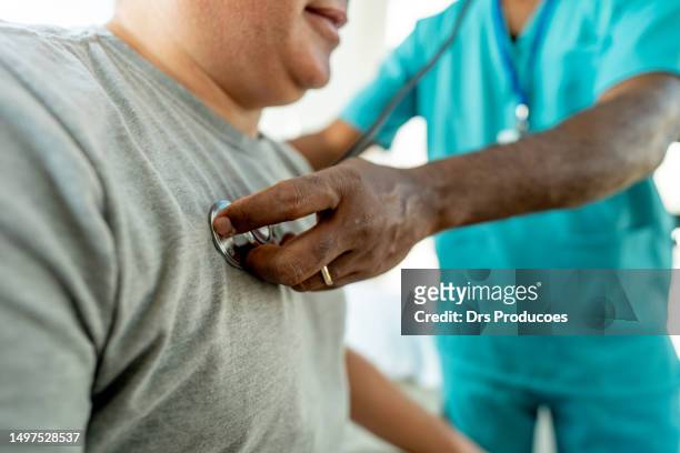 uomo maturo che controlla la sua pressione sanguigna in uno studio medico - listening to heartbeat foto e immagini stock