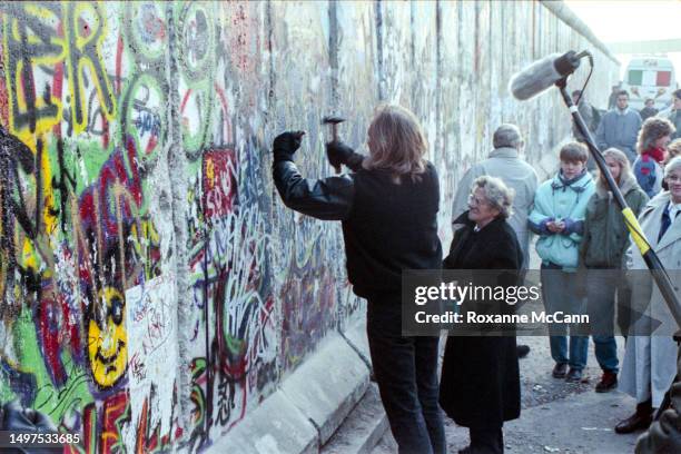 Man chips away at the Berlin Wall with a hammer and chisel surrounded by a crowd and a microphone on November 12, 1989 in Berlin, Germany.