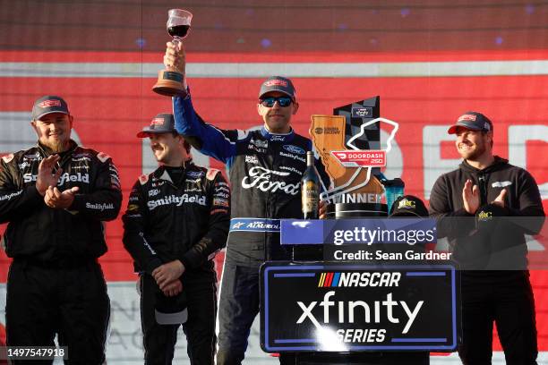 Aric Almirola, driver of the Michael Roberts Construction Ford, celebrates with wine in victory lane after winning the NASCAR Xfinity Series DoorDash...