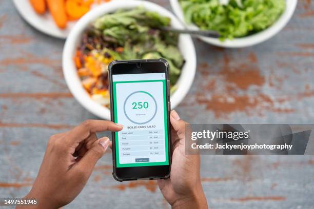 young woman eating salad while using calorie counter app on smartphone - dieta-de-baixos-carboidratos - fotografias e filmes do acervo