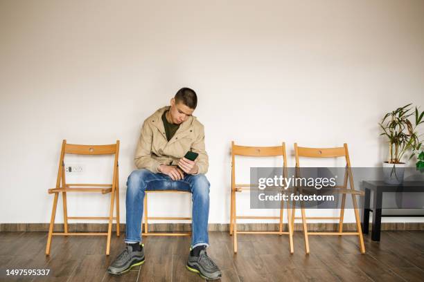 teenage boy sitting on a chair in a waiting room, waiting - one teenage boy only stock pictures, royalty-free photos & images