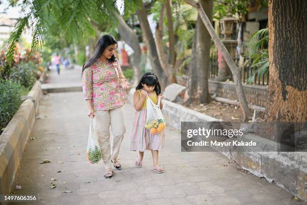 mother and daughter walk along footpath with bags of vegetables and fruits - man made object stock pictures, royalty-free photos & images