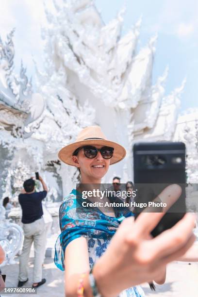portrait of a smiling woman taking a selfie with her mobile phone at the white temple in chang rai - chiang rai province stock pictures, royalty-free photos & images