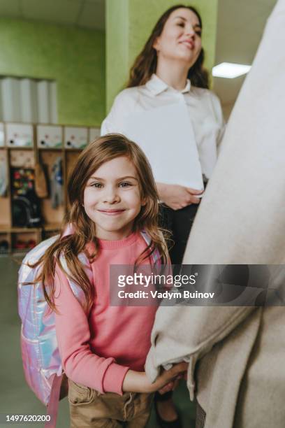 elementary school student looking at camera while teacher talking to her mother at first day in school - schulbeginn stock-fotos und bilder