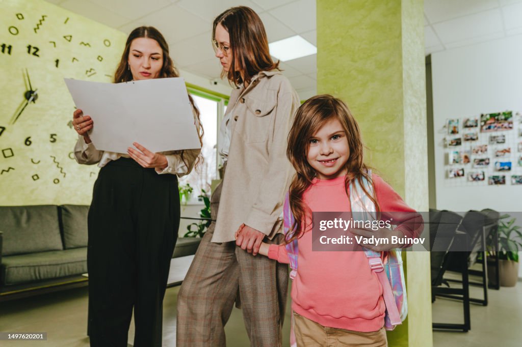 Elementary school student looking at camera while teacher talking to her mother at first day in school