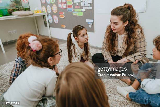 schoolchildren with their teacher sitting on the floor in circle in a classroom - children circle floor stock pictures, royalty-free photos & images