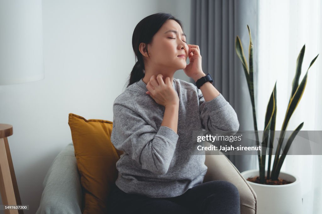 Asian woman irritate itching dry skin scratching her skin sitting on armchair in living room at home.