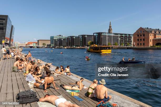 People enjoying sun bathing alongside the wharf near the Royal Library extension from 1999, Den Sorte Diamand seen on June 5, 2023 in Copenhagen,...