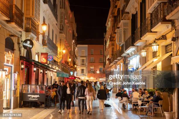 People sit dine and drink outside restaurants and bars on the street at night in the old town on April 21, 2023 in Malaga, Spain.