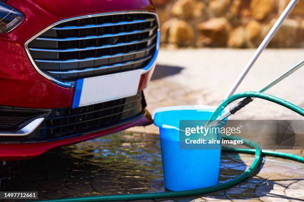 a ground perspective of a car beside a blue bucket and a hoe water splatted on the ground - volume fluid capacity stock pictures, royalty-free photos & images