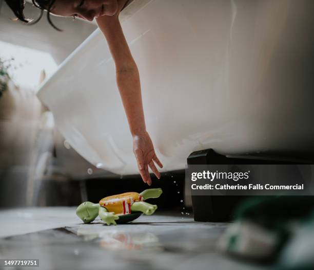 a little girl reaches for a bath toy she has dropped out of a freestanding bath - free standing bath stock pictures, royalty-free photos & images