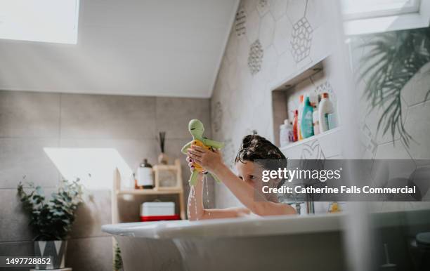 a child plays with a plastic tortoise bath toy` in a roll top bath in a domestic bathroom - steam bath home stock pictures, royalty-free photos & images
