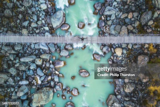 looking down on young happy man on suspension bridge over glacial river in the mountains - nieuw zeeland stockfoto's en -beelden