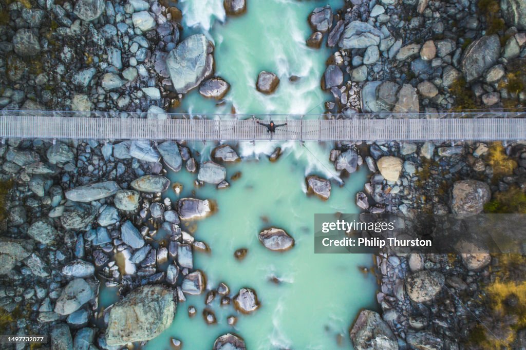 Olhando para baixo no jovem feliz na ponte suspensa sobre o rio glacial nas montanhas