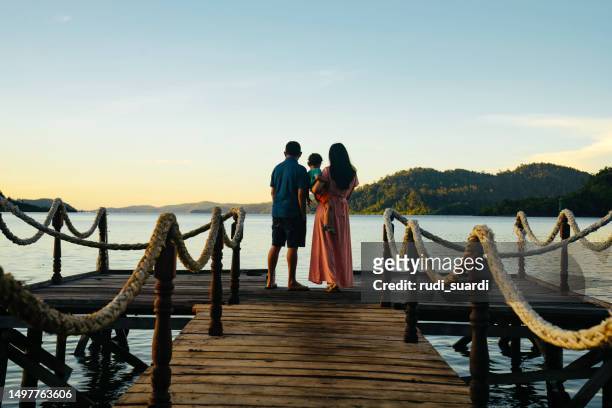 asian couple carrying son on jetty at sunrise, - vista posterior stock pictures, royalty-free photos & images
