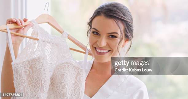 happy bride preparing for her luxury wedding in a hotel room while holding her beautiful dress. portrait of a woman with trendy hair, makeup and a smile in a gown while getting ready for marriage. - wedding dress on hanger stock pictures, royalty-free photos & images