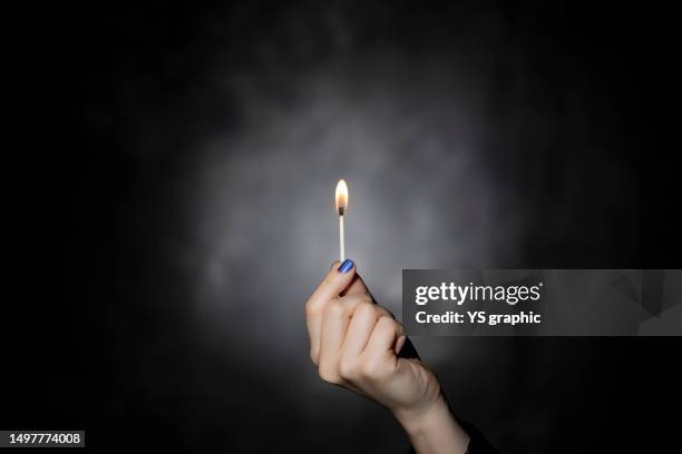 woman's hand holding lit match on black background. - match lighting equipment stock pictures, royalty-free photos & images