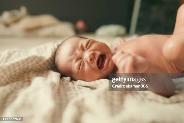 facial expression negative emotion asian newborn baby crying and lying down on the bed  during  mother changing cloth and baby diaper - black premature babies stock pictures, royalty-free photos & images