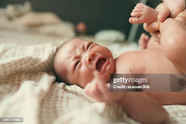 facial expression negative emotion asian newborn baby crying and lying down on the bed  during  mother changing cloth and baby diaper - black premature babies stock pictures, royalty-free photos & images