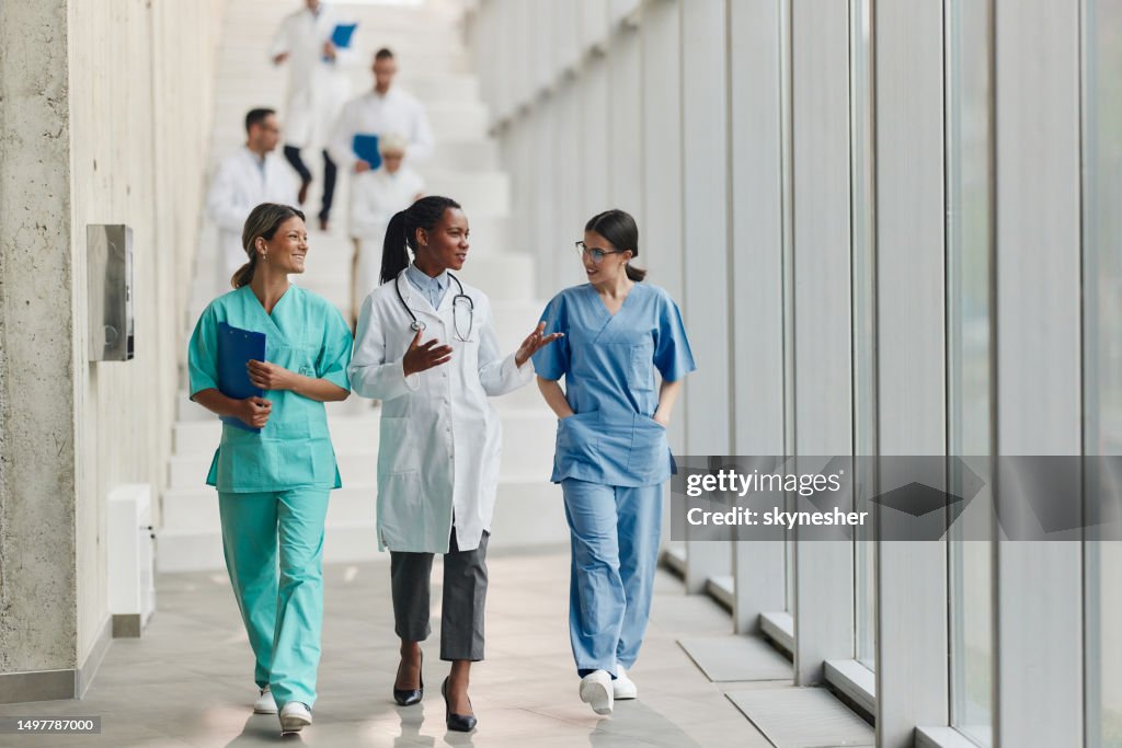Glückliche Ärztinnen, die unterwegs in einem Krankenhaus sprechen.