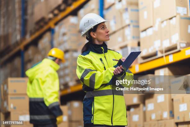 female warehouse worker with clipboard checking delivery, stock in warehouse. - zona industrial imagens e fotografias de stock