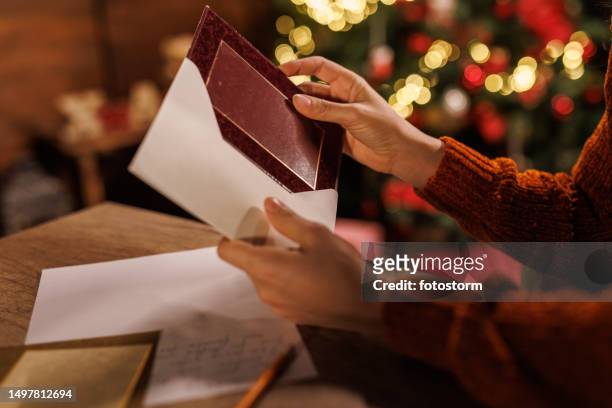 young woman putting a christmas card in an envelope - holiday message stock pictures, royalty-free photos & images