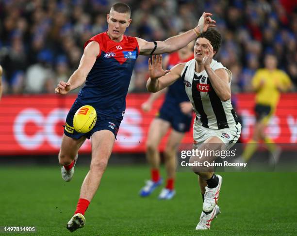 Adam Tomlinson of the Demons kicks whilst being tackled by Brody Mihocek of the Magpies during the round 13 AFL match between Melbourne Demons and...