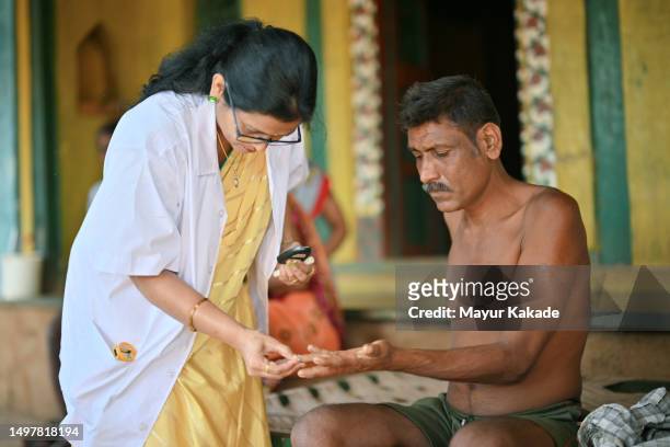 doctor diligently checking the blood sugar levels of a male patient using a glucometer during a rural health care camp - maharashtra stockfoto's en -beelden