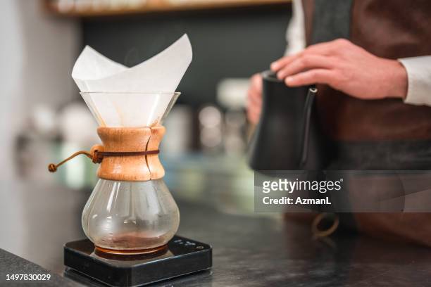 kaukasisches männliches barista-wasser, das über frisch gemahlenen kaffee in einer cafeteria gießt - filterkaffee stock-fotos und bilder