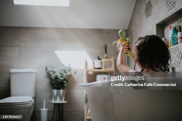 a child, with soapy hair, and a plastic bath toy, enjoys a warm bath. - free standing bath stock pictures, royalty-free photos & images